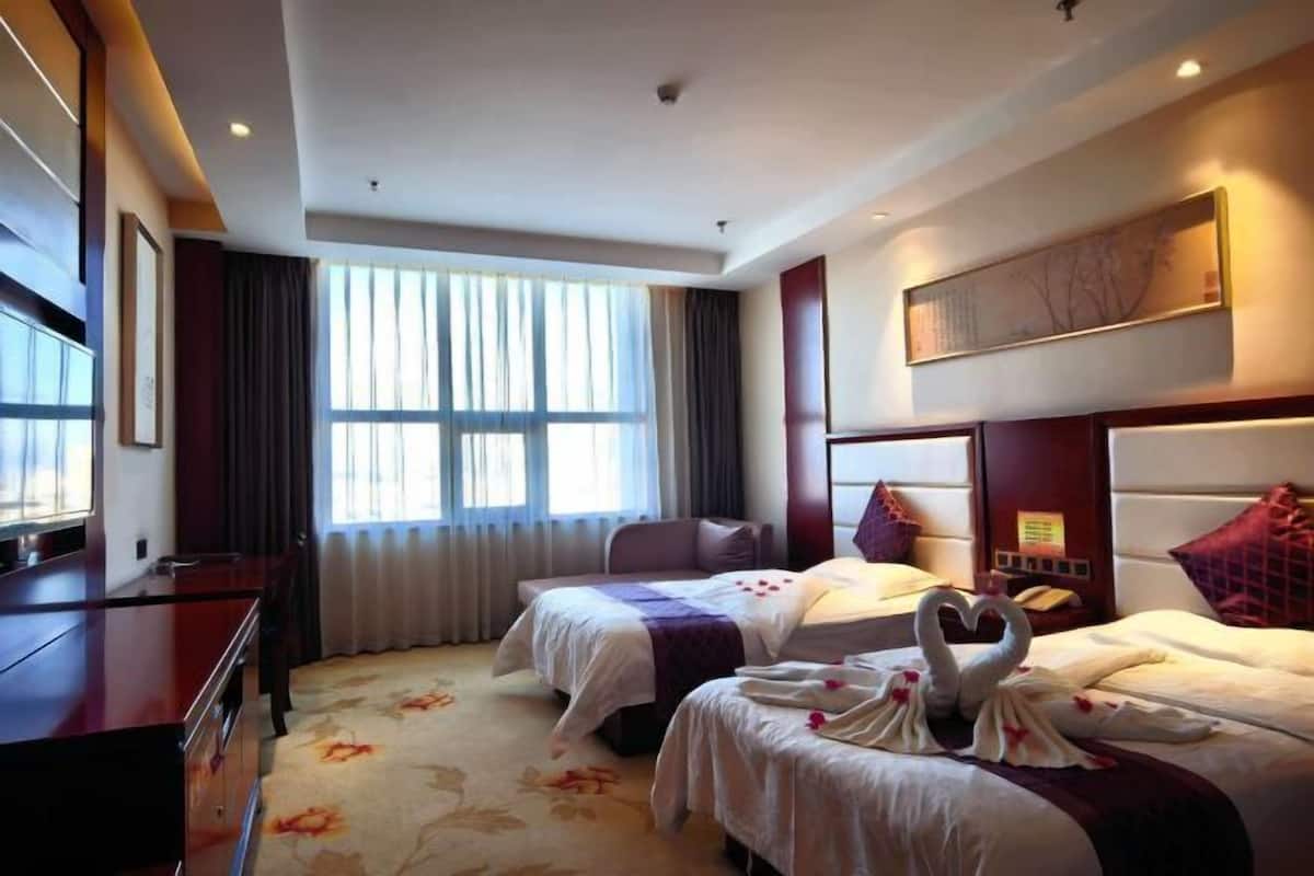 A hotel room with two beds, a desk, a TV, and a large window.