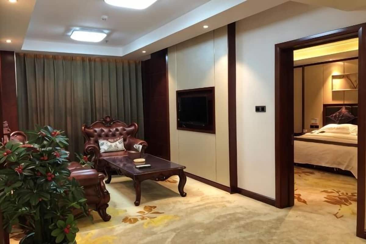 A hotel room with a large bed, a TV mounted on the wall, a wooden coffee table, and a potted plant.