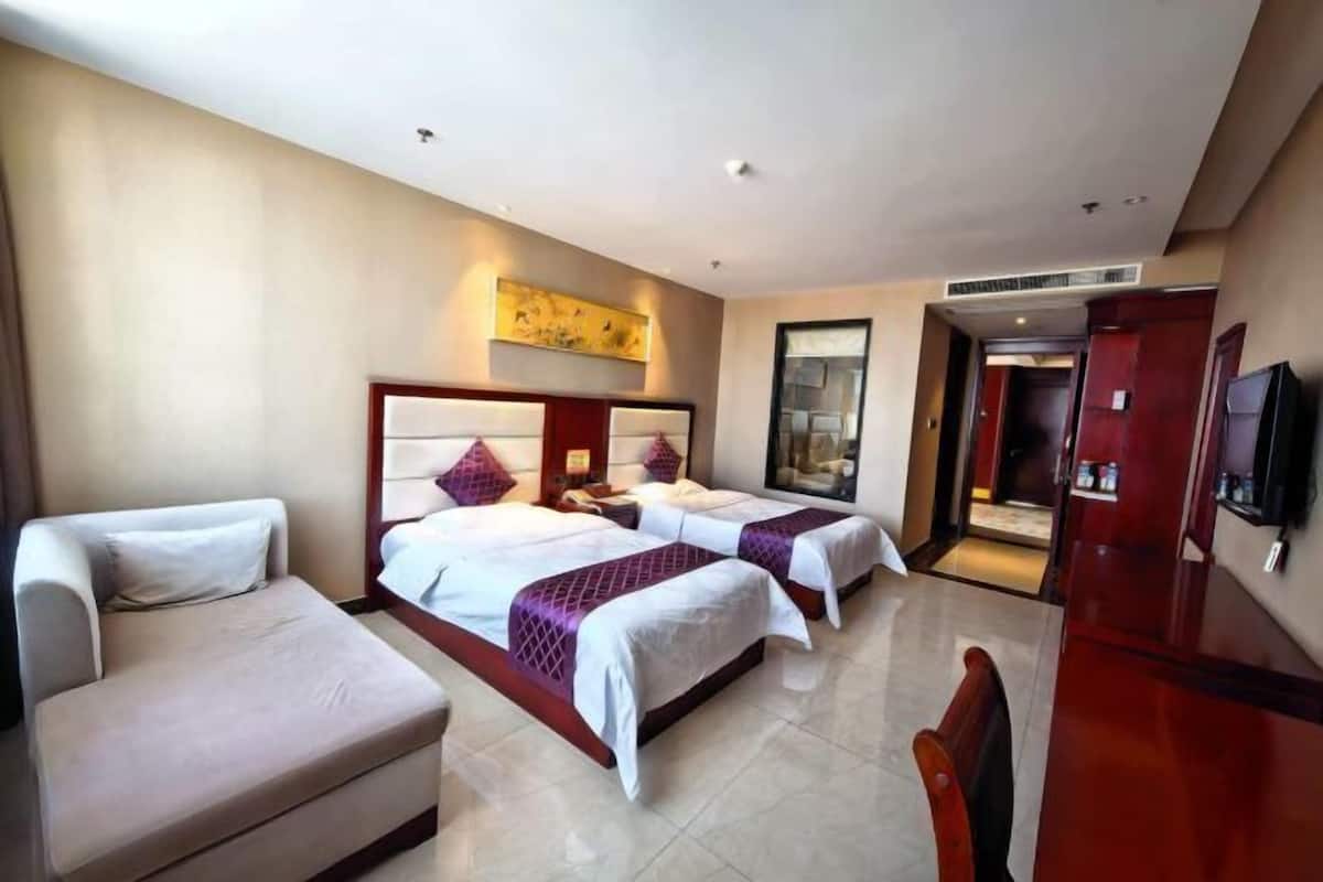 A hotel room with two beds, a sofa, a TV, and a painting on the wall.