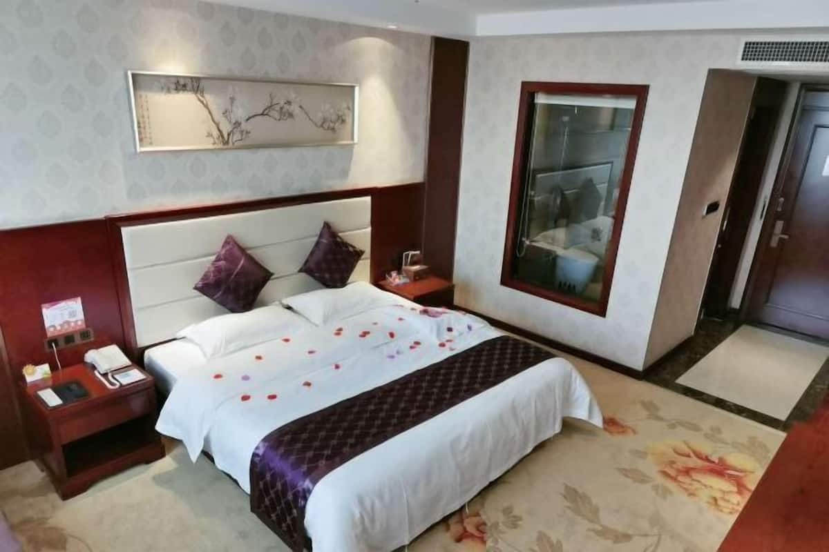 A hotel room with a large bed, a nightstand, a bedside table, a wall-mounted artwork, and a large window.