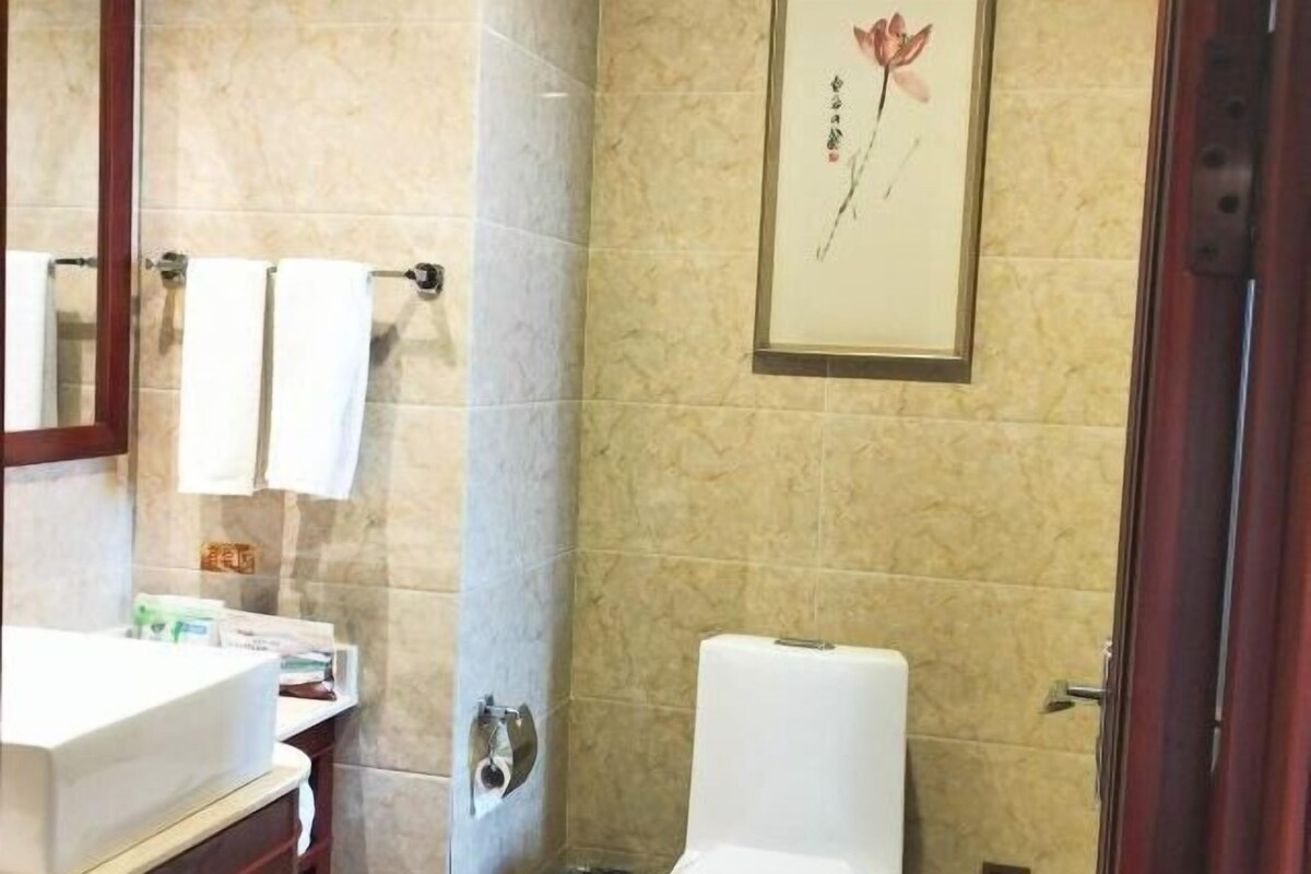 A bathroom with a toilet, a sink, and a mirror. There is a framed picture on the wall.
