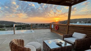 An outdoor seating area with wicker furniture and a glass table, overlooking a scenic landscape with a sunset. - Phaestias Terra Villas (Faistos)