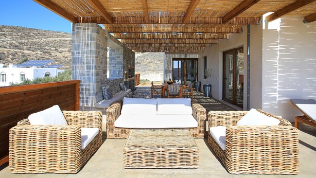 A covered outdoor seating area with wicker furniture and a stone wall. - Phaestias Terra Villas (Faistos)