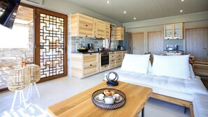 A modern hotel room with a wooden dining table, a sofa, a kitchen area, and a balcony with wicker chairs. - Phaestias Terra Villas (Faistos)