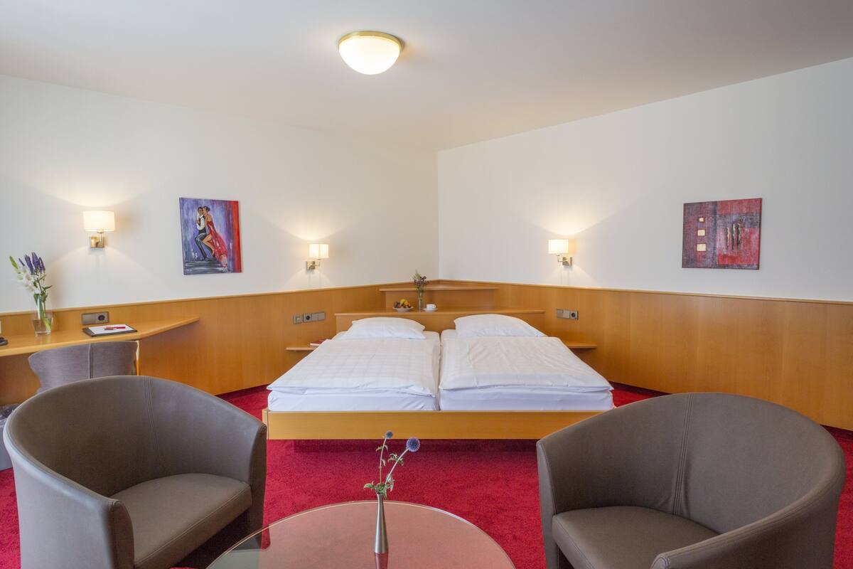 Een hotelkamer met een bed, twee fauteuils, een bureau en een bloemenvaas.