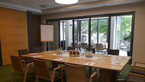 A conference room with a large table, chairs, a whiteboard, and a view of the outdoors through large windows.