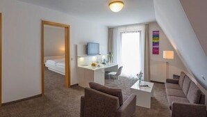 A hotel room with a bed, a desk with a computer, a TV, and a seating area with chairs and a sofa.
