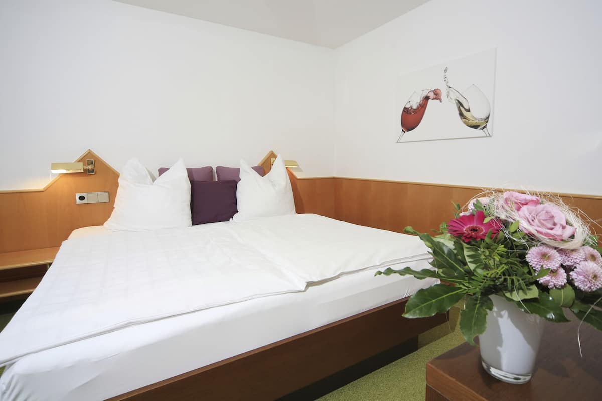 Een net opgemaakt bed met witte lakens, een houten hoofdbord en een nachtkastje met een bloemenvaas.