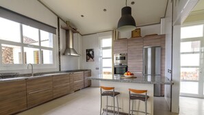 Une cuisine moderne dotée d’un grand îlot central, d’appareils électroménagers en acier inoxydable et offrant une vue sur l’extérieur.