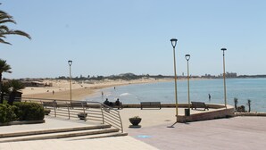 Eine Uferpromenade mit Bänken, einem Gehweg und Blick auf Strand und Meer.