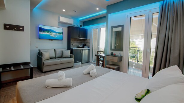 A modern hotel room with a bed, a sofa, a desk, a TV, and a balcony with curtains. - Dim House (Parga)