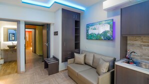 A modern living room with a sofa, a built-in kitchen area, and a hallway leading to a bathroom. - Dim House (Parga)