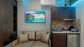 A compact living space with a sofa, a kitchen area, and a mounted TV displaying a scenic view. - Dim House (Parga)