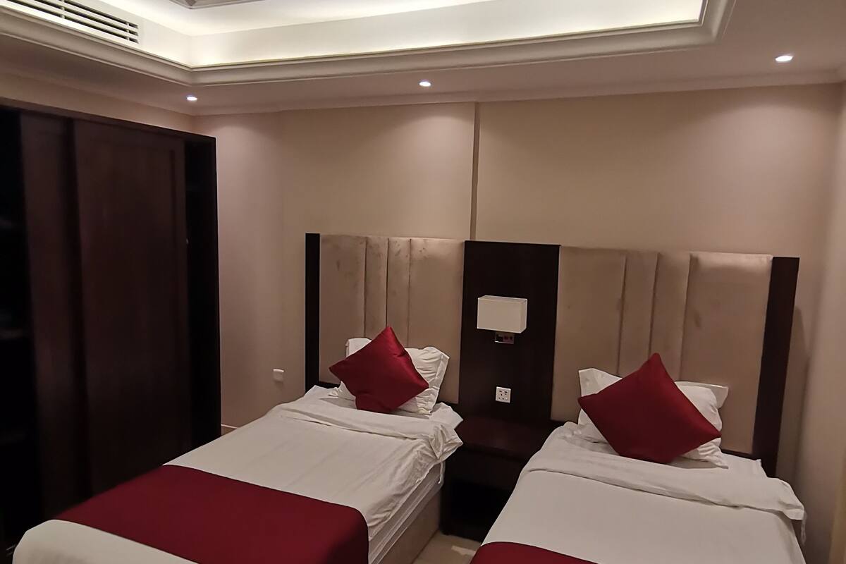Una habitación de hotel con dos camas, cada una con una colcha roja y blanca, un cabecero de madera y una mesita de noche con una lámpara.