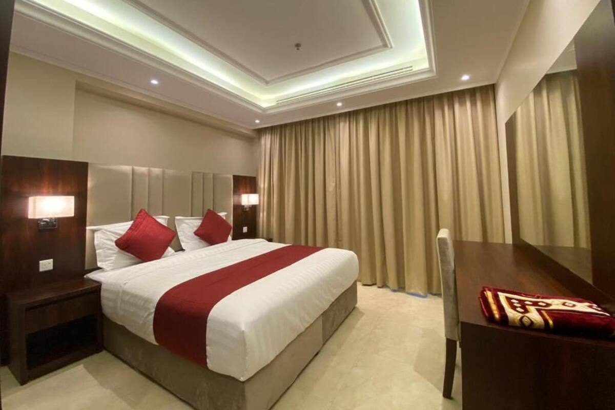 Habitación de hotel con una cama grande, dos mesitas de noche con lámparas, un escritorio con silla y un ventanal con cortinas.