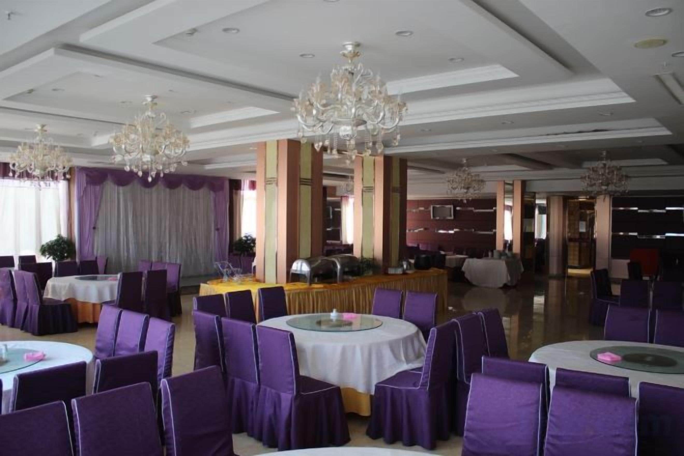 A banquet hall with round tables and purple chairs, chandeliers, and a stage area.