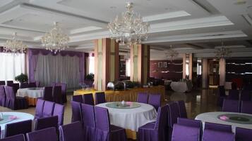 A banquet hall with round tables and purple chairs, chandeliers, and a stage area.