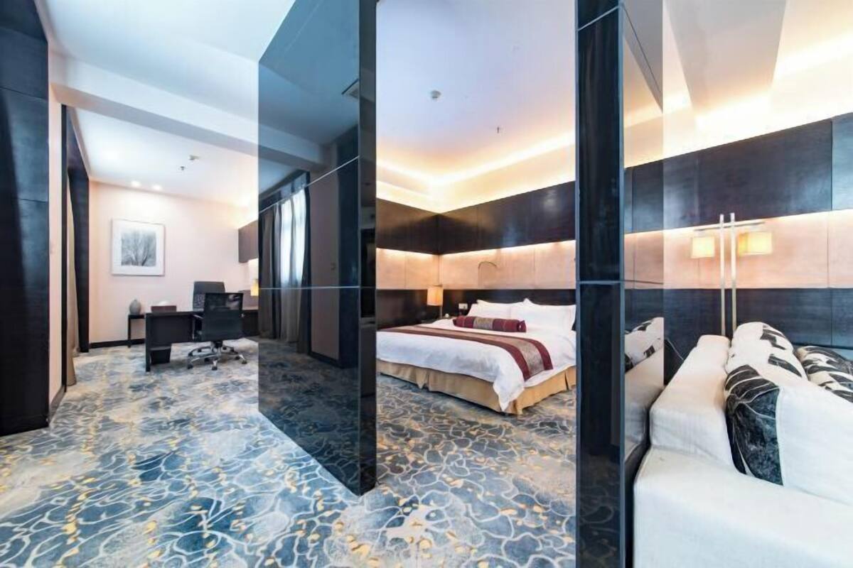 A modern hotel room with a large bed, a desk, and a sofa.