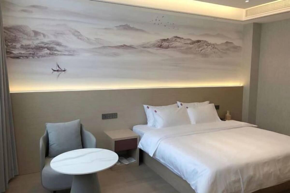 A hotel room with a bed, a chair, a small table, and a wall with a painting.