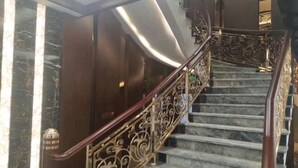 Un escalier en marbre, agrémenté de rampes en métal ouvragé et d’une main courante en bois.