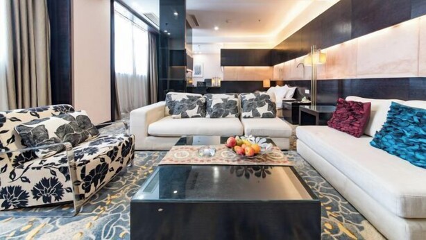 Une chambre d’hôtel moderne avec un canapé, une table basse sur laquelle se trouvent des fruits, et une vue sur la cuisine.