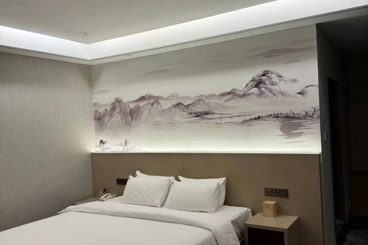 A hotel room with a bed, a nightstand, a wall-mounted artwork, and a ceiling light.