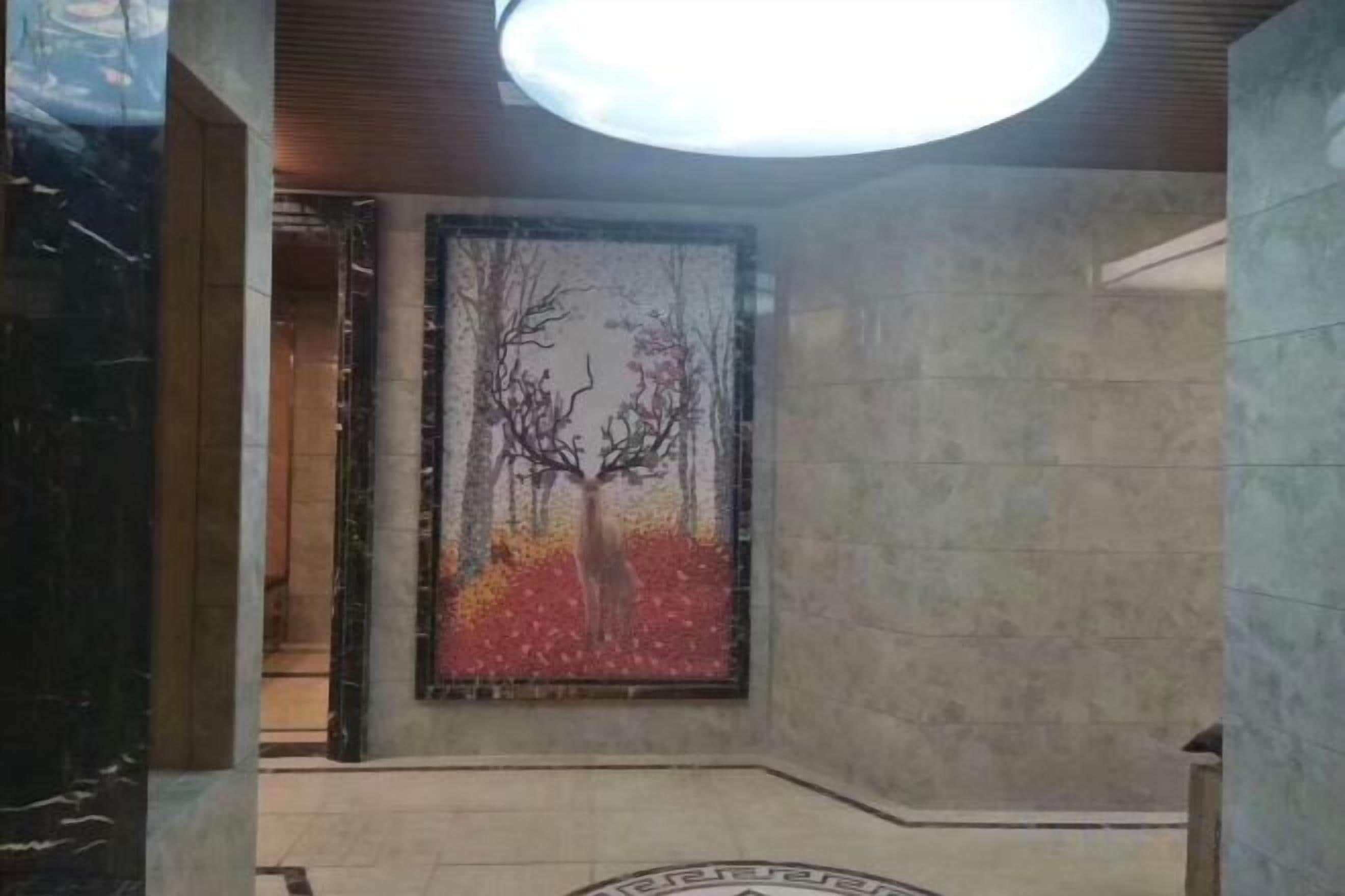 A lobby with a large abstract painting, a circular emblem on the floor, and a ceiling light fixture.