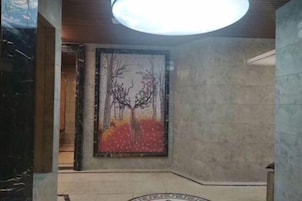 Un vestíbulo con un cuadro abstracto de gran tamaño, un emblema circular en el suelo y una lámpara en el techo.