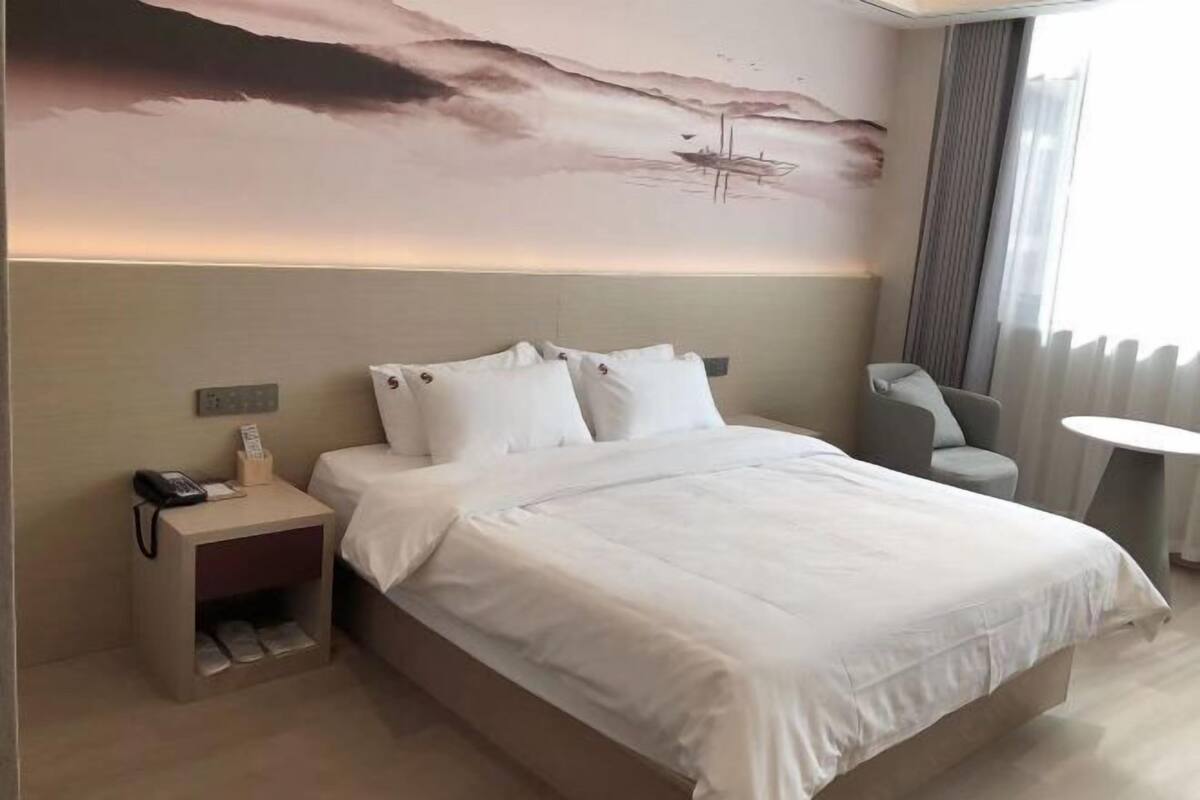 A hotel room with a bed, a nightstand with a phone, a chair, and a small table.