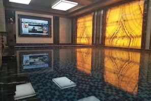 A spacious indoor swimming pool with a checkered floor, a large screen displaying content, and a wall with a wood-like pattern.