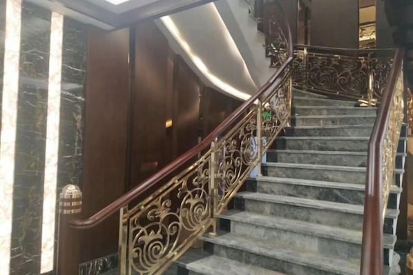 A marble staircase with ornate metal railings and a modern light fixture.