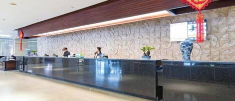 A reception area with a marble wall, a reception desk, and a red decorative hanging.
