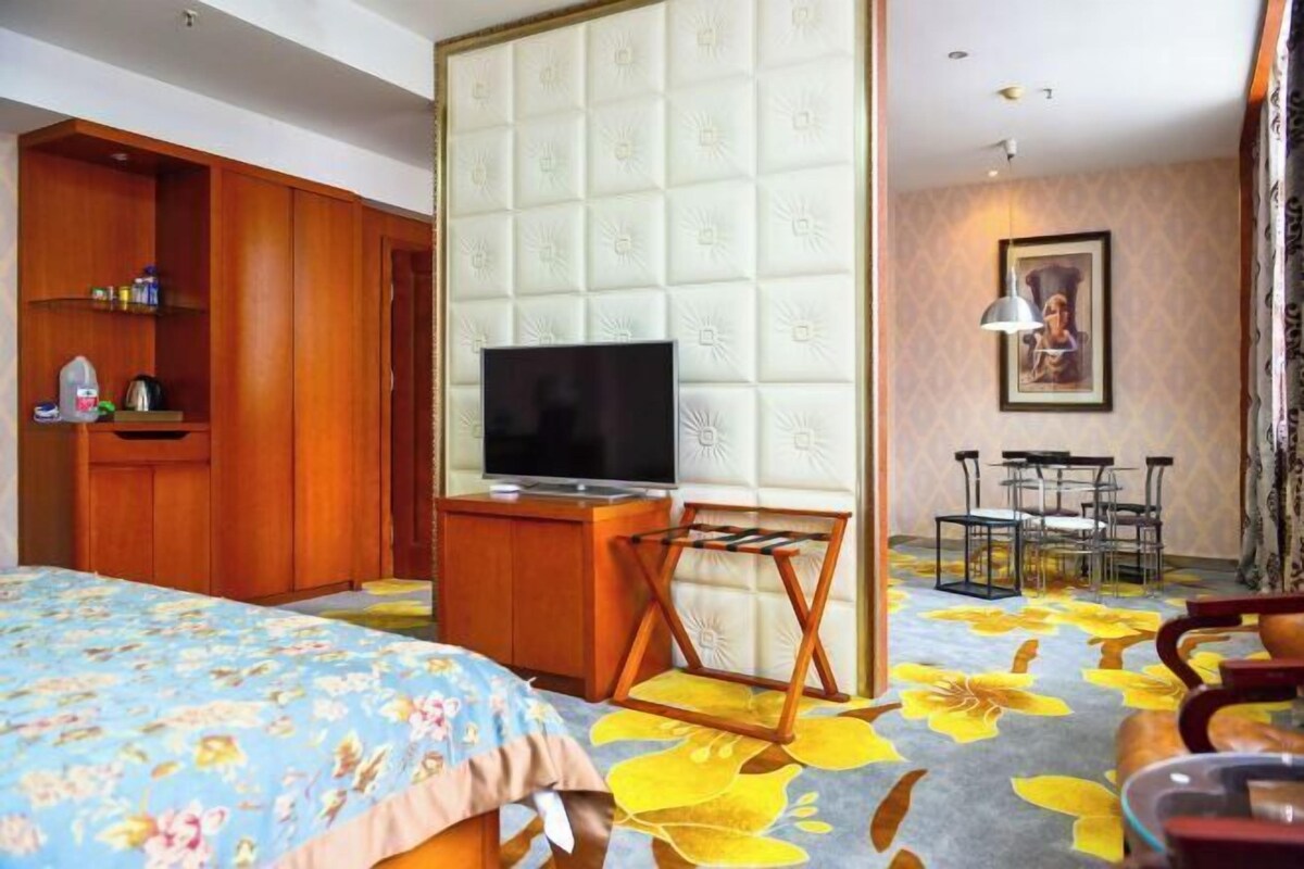 A hotel room with a bed, a TV, a wooden wardrobe, a small table, and a chair.
