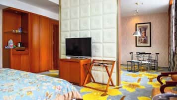 A hotel room with a bed, a TV, a wooden wardrobe, a small table, and a chair.