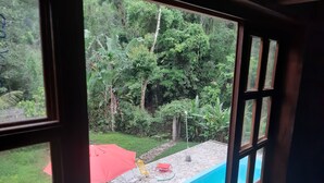 A view of a swimming pool with a stone border, surrounded by a grassy area and lush greenery. - Chalé Vagalume em Boiçucanga (São Sebastião)