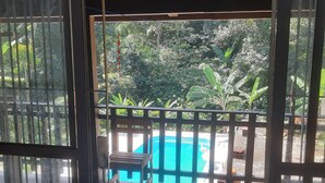 A view from a room with a sliding glass door to an outdoor area with a pool, a wooden deck, and surrounding greenery. - Chalé Vagalume em Boiçucanga (São Sebastião)