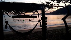 A beach scene with a hammock and a thatched roof structure. - Chalé Vagalume em Boiçucanga (São Sebastião)