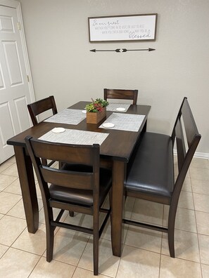 Una mesa de comedor con cuatro sillas, una planta pequeña y un letrero en la pared.