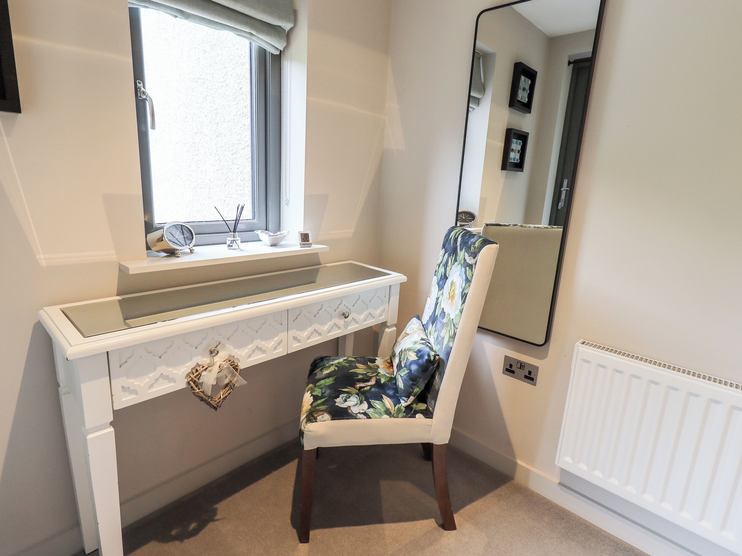 Un baño con tocador blanco, un espejo y una silla con estampado floral.