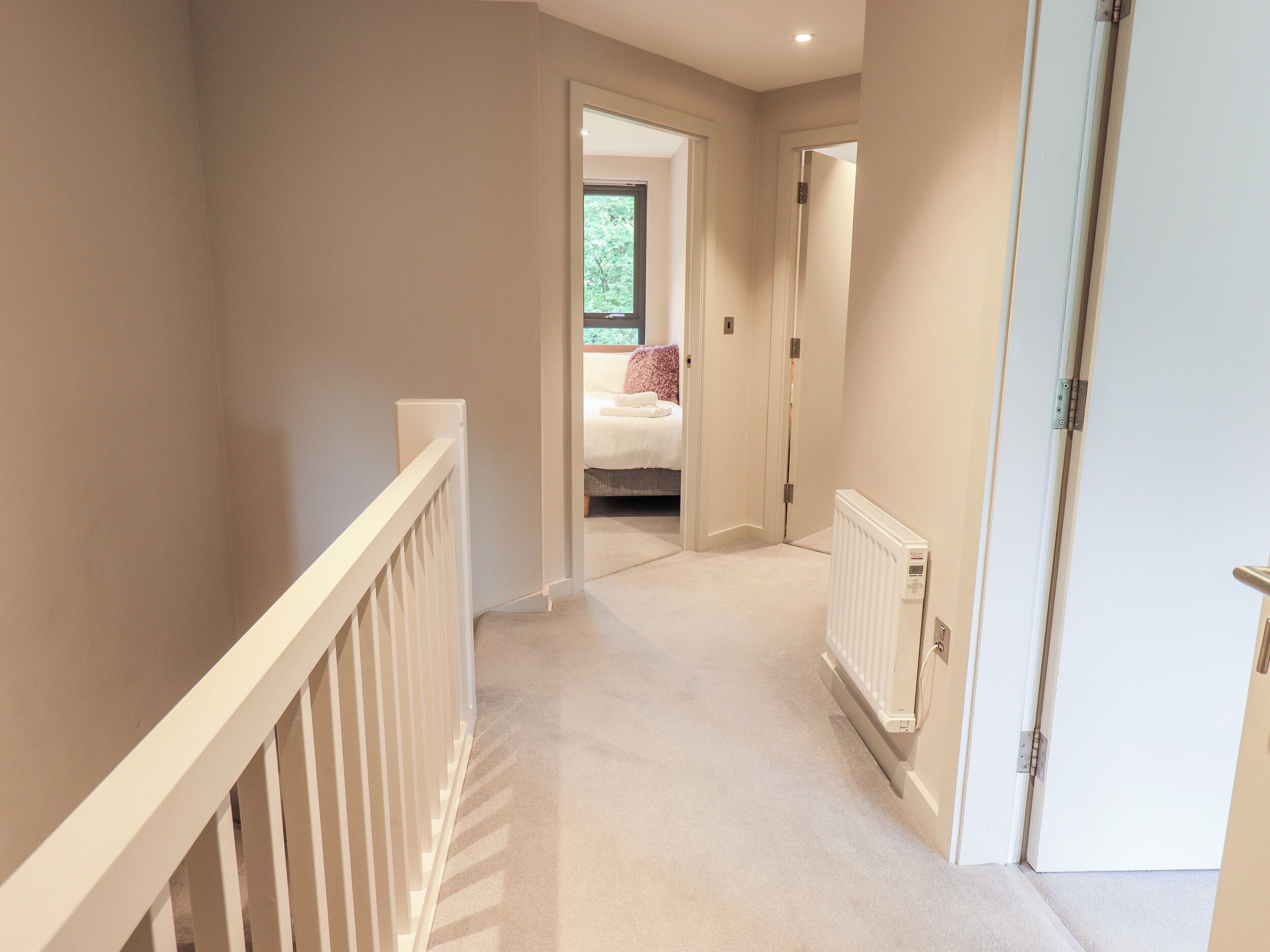 A hallway with a white railing, a radiator, and a door leading to a bedroom with a bed and a window.