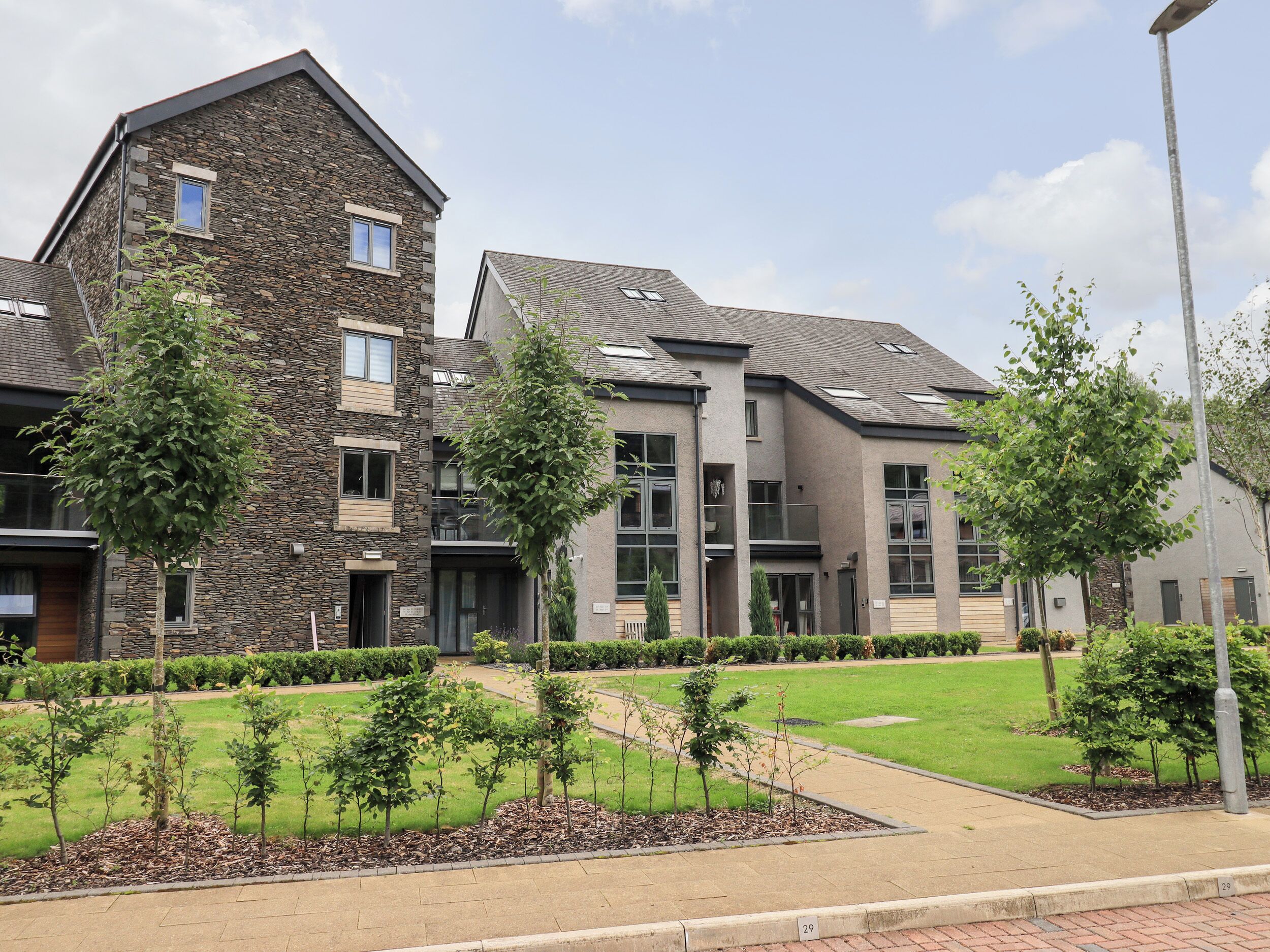 A modern building with stone and concrete facades, multiple windows, and a well-maintained lawn with young trees.