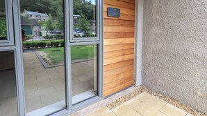 Entrada de un edificio con un revestimiento de madera, un letrero con el número 24, y vistas a un estacionamiento y áreas verdes.