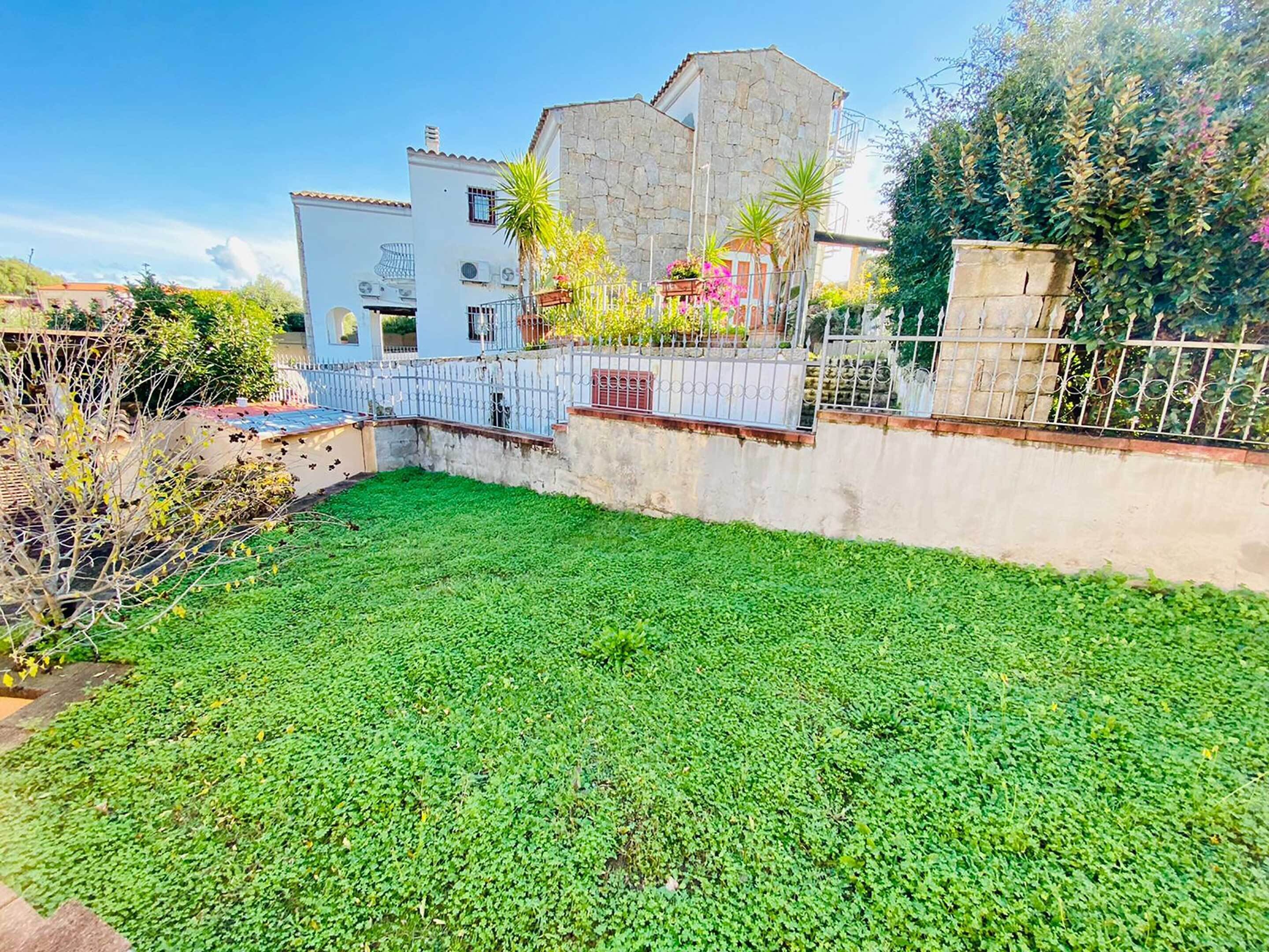Une cour avec une pelouse, un mur de pierre et un bâtiment blanc doté d’un balcon.