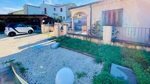 A residential area with a white car parked in a driveway, a house with a tiled roof, and a clear sky. - Casa Vacanza Silvaredda (San Teodoro)