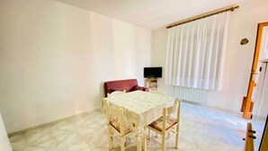 A dining area with a table and chairs, a television on a stand, and a window with curtains. - Casa Vacanza Silvaredda (San Teodoro)