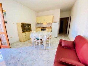 Un espacio habitable compacto con una mesa y sillas de comedor, una zona de cocina con armarios y electrodomésticos, y una silla roja en primer plano.