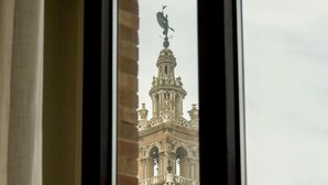A view of a historic building with intricate architectural details through a window with a metal railing. - U-Sense Sevilla Catedral (Seville)
