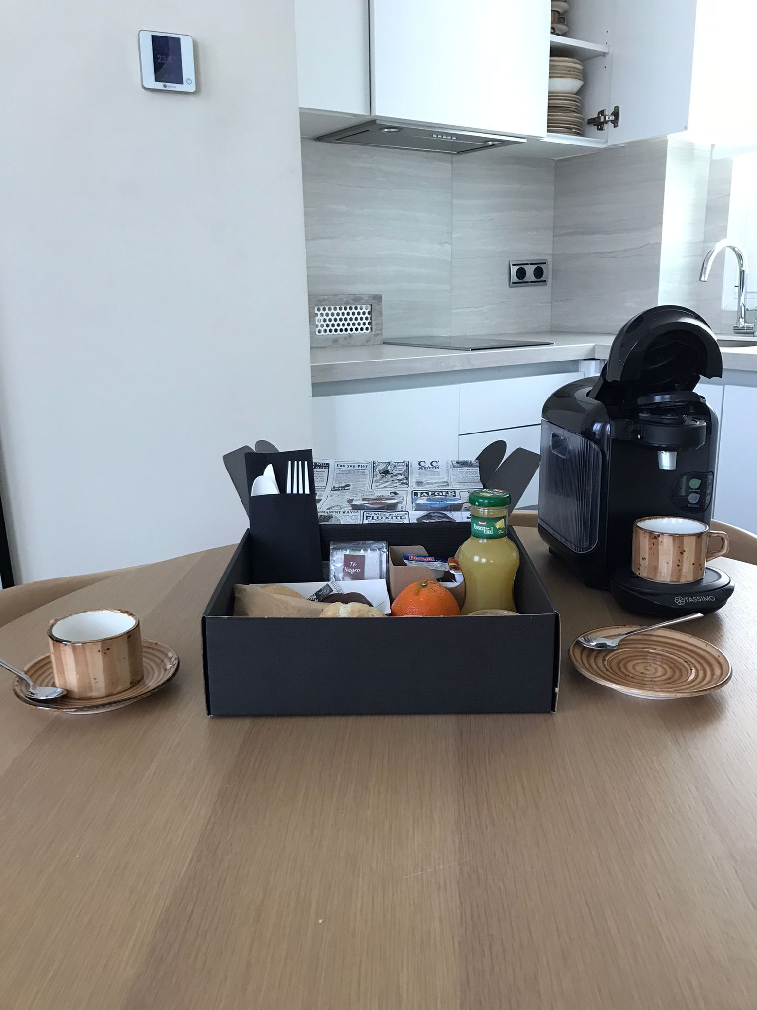 Uma cozinha moderna com cafeteira, uma caixa de itens de café da manhã e uma xícara de café sobre uma mesa.