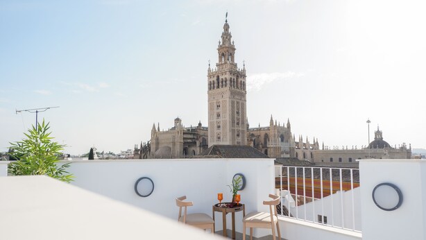 A terrace with two chairs and a small table, overlooking a historic building with a tall tower. - U-Sense Sevilla Catedral (Seville)