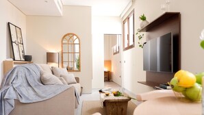 A modern living room with a sofa, a coffee table, and a TV. There is a window with a view of the outside. - U-Sense Sevilla Catedral (Seville)